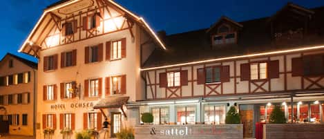 A traditional European hotel with a well-lit facade, a visible entrance, and a sign for a restaurant named "sattelschnecke".