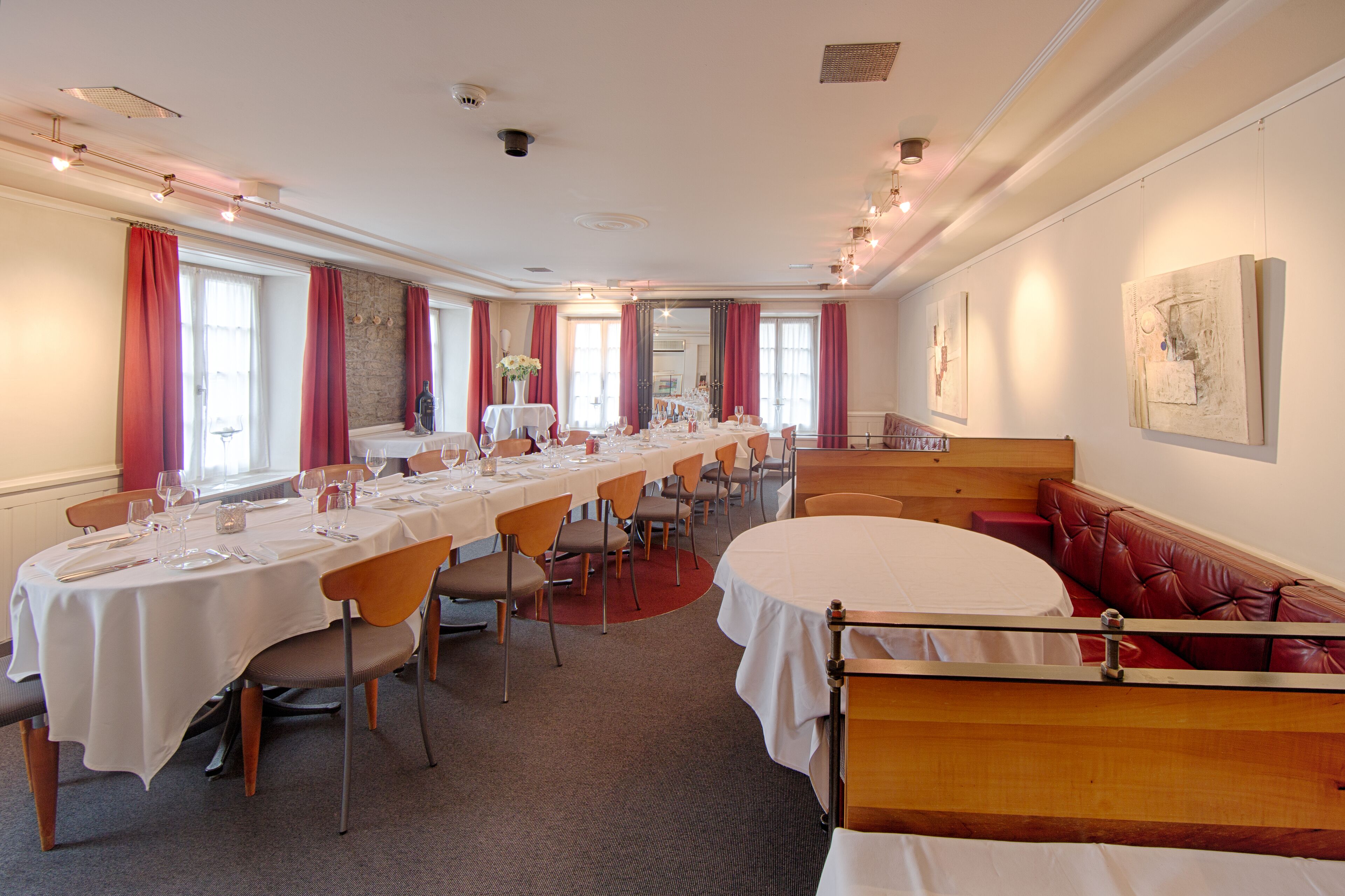 A conference room with long tables set for a meeting, a red leather sofa, and artwork on the walls.