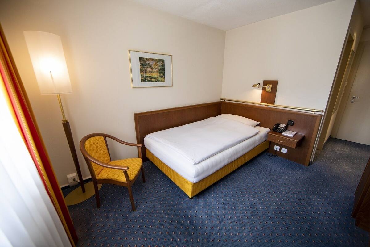 Een hotelkamer met een bed, een stoel, een bureau met telefoon en een schilderij aan de muur.