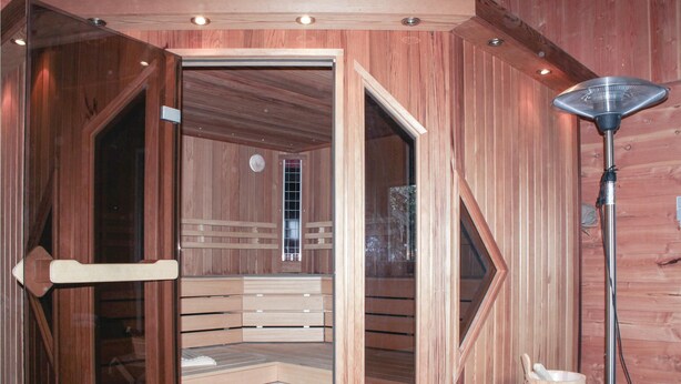 Een sauna met houten banken en een glazen deur, een heater en een emmer.