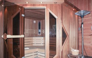 Una sauna con panche in legno e una porta in vetro, una stufa e un catino.