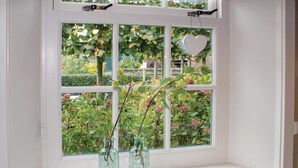 Een raam met twee glazen flessen met planten, een hartvormige decoratie en uitzicht op groen buiten.