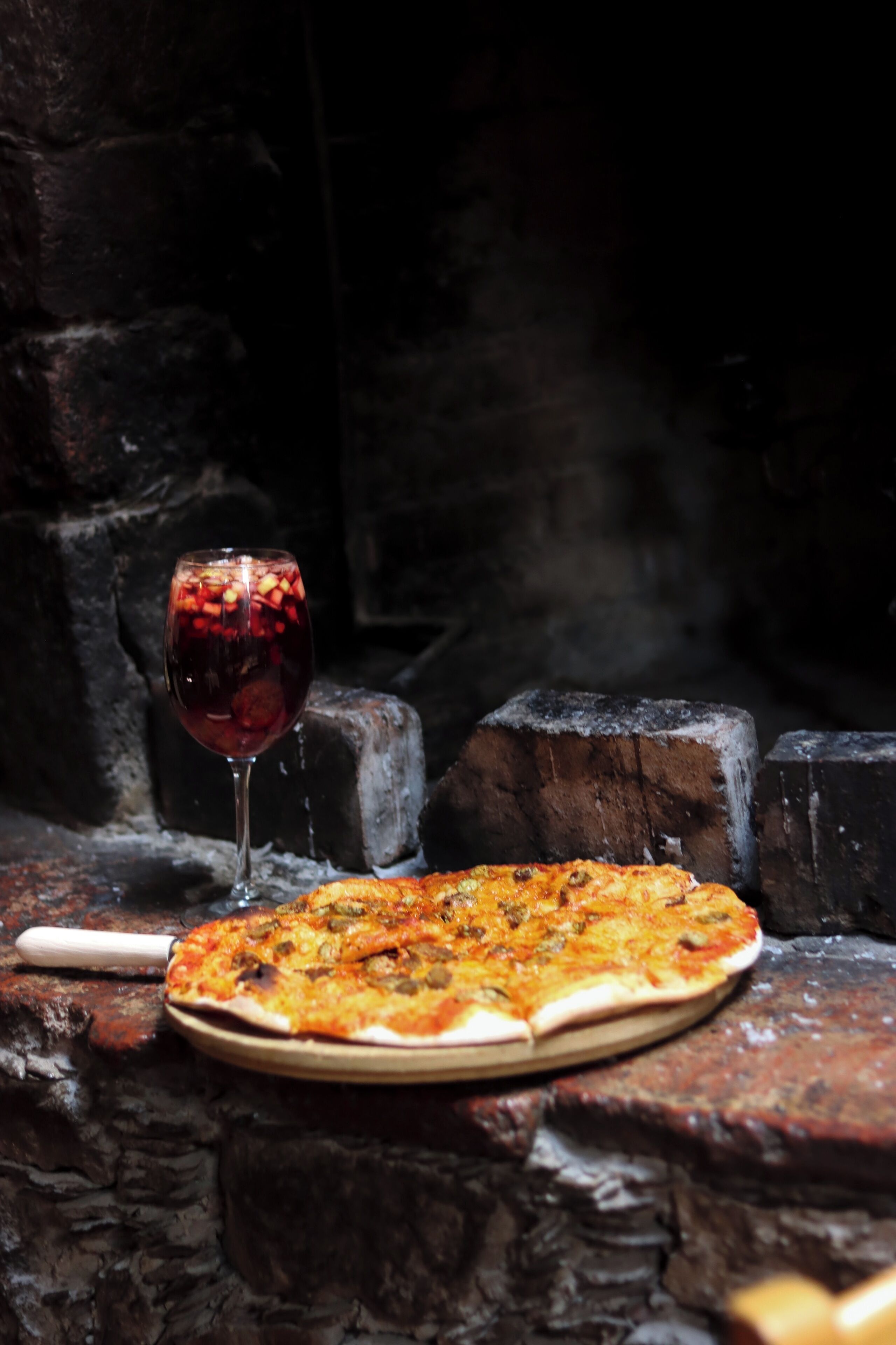 Eine Pizza auf einem Holzboden, im Hintergrund ein Glas Rotwein.