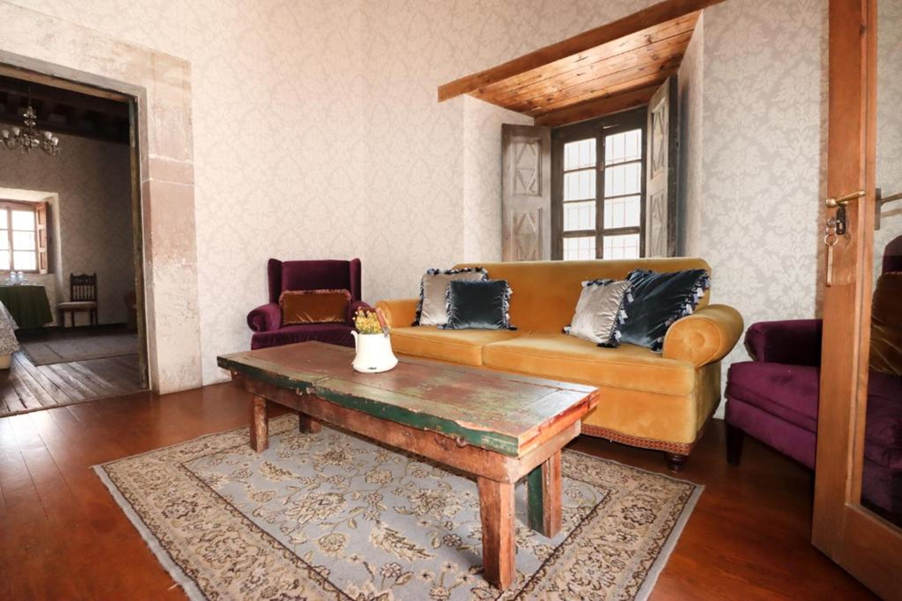 Un salon chaleureux avec une table basse en bois, un canapé jaune agrémenté de coussins à motifs et un fauteuil violet.