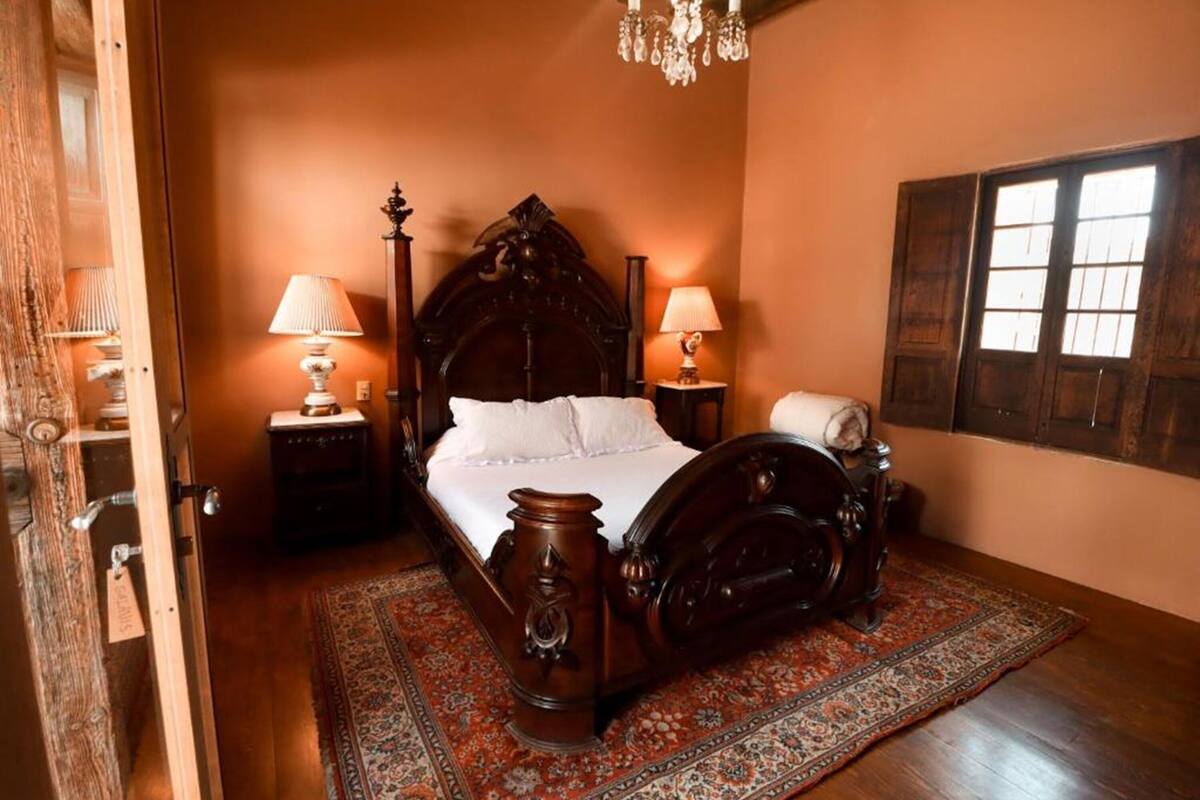 Une chambre à coucher de style traditionnel, avec un grand lit, deux tables de chevet, un lustre et une fenêtre avec des volets.