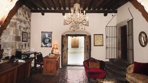 Una habitación rústica con techo de madera, una araña, un sillón rojo, un sofá y una pared de piedra.