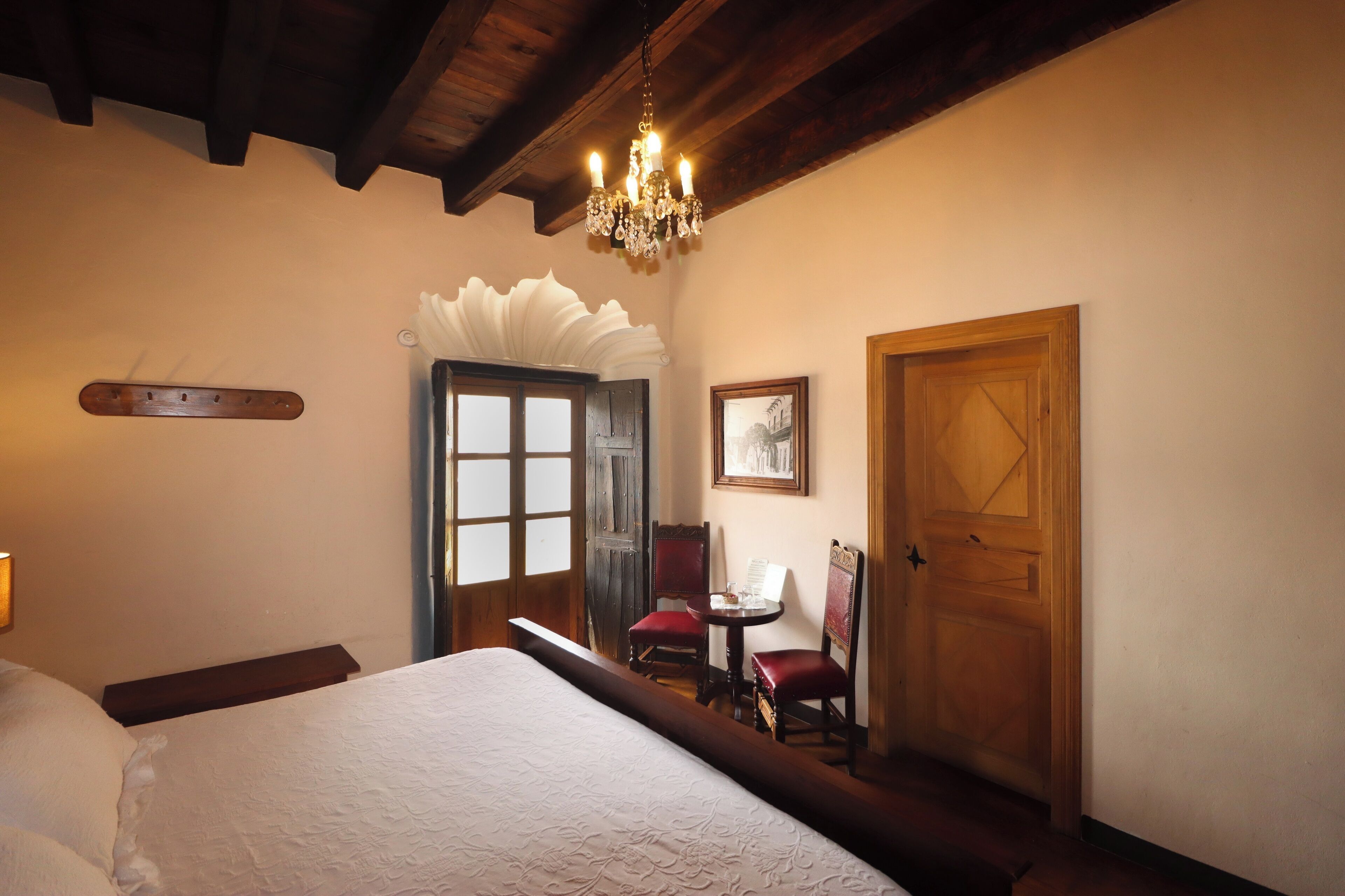 Une chambre à coucher avec un grand lit, un lustre, une porte en bois et une petite table avec des chaises.