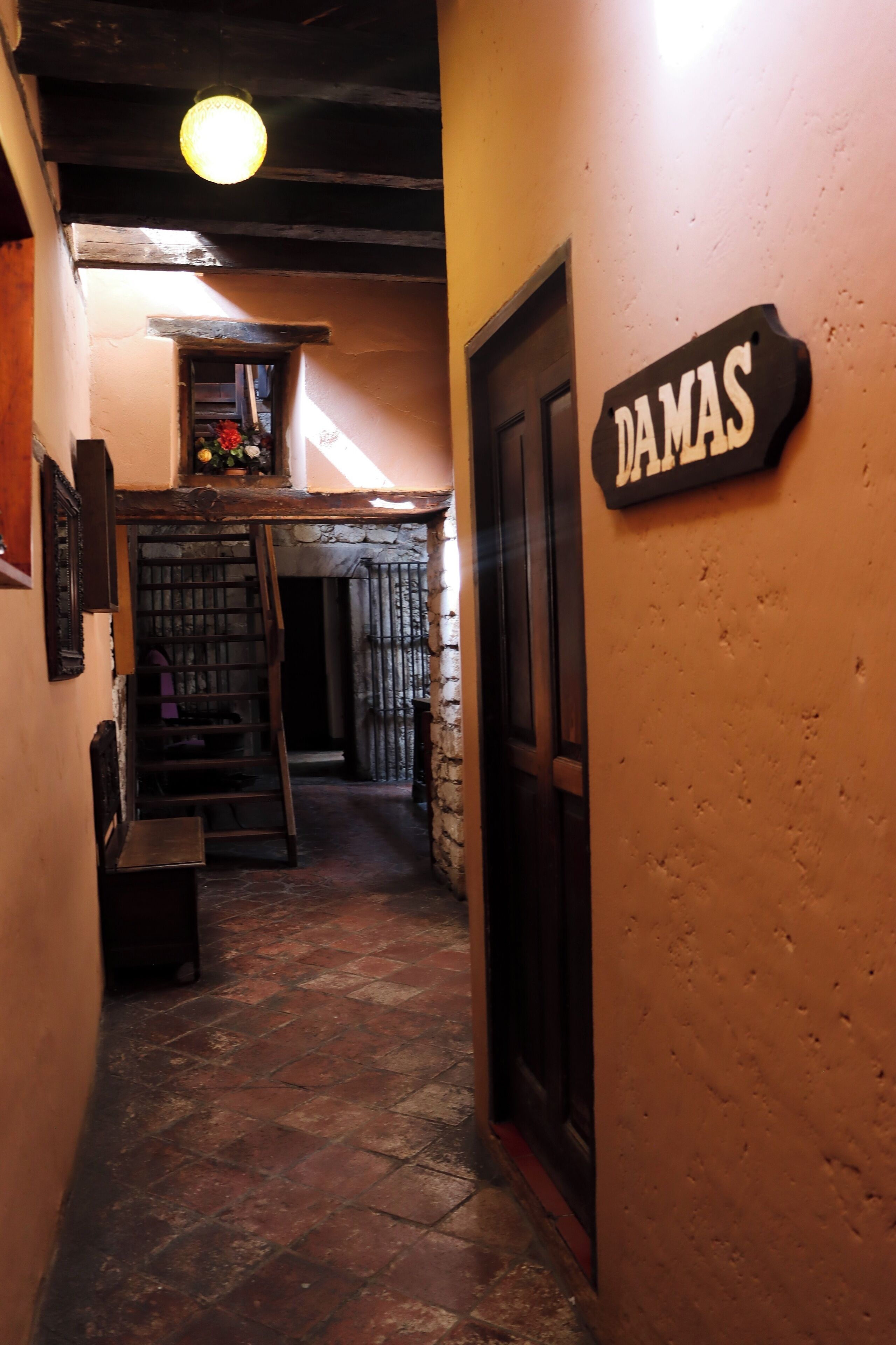A narrow hallway with a wooden door labeled "DAMAS" and a staircase leading to an upper level.