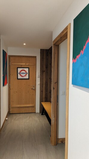 A hallway with a wooden door labeled 'SWISS COTTAGE,' a bench, and a wall with a blue abstract painting.