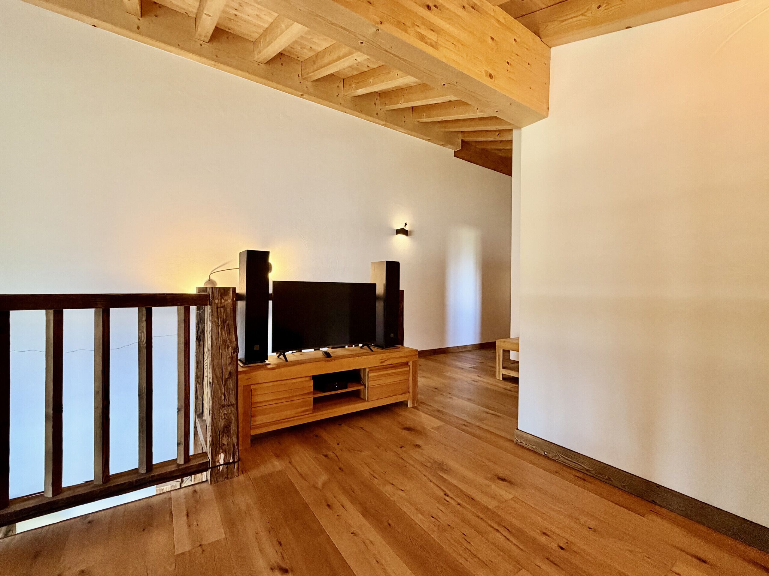 Une pièce dotée d’un plancher en bois, d’un meuble pour la télévision avec un écran plat, d’une rambarde en bois et d’un luminaire fixé au mur.