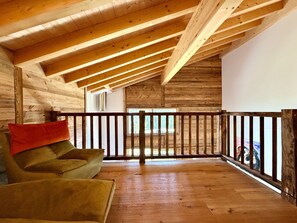 A wooden interior with a high ceiling, a wooden railing, and a view through a window.
