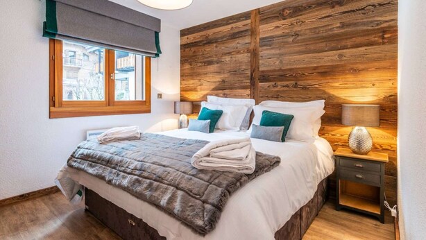 Un dormitorio con cabecera de madera, cama grande con sábanas blancas, almohadas color turquesa y una manta suave.