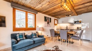 Una sala de estar moderna con un sofá azul, un comedor con sillas, una cocina con armarios blancos y un techo de madera.