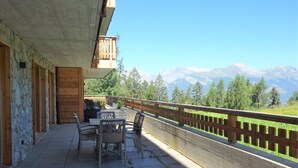 Ein Balkon mit Tisch und Stühlen mit Blick auf eine gebirgige Landschaft.