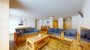 Ein gemütlicher Wohnbereich mit Holzmöbeln, darunter Sofas und ein Couchtisch, sowie ein Essbereich mit Holzsesseln und einem Tisch.