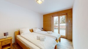 Ein Schlafzimmer mit zwei Betten, Holzwänden, einem kleinen Nachttisch mit Lampe und Blick durch eine Glastür nach draußen.