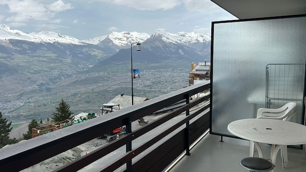 A balcony with a view of snow-capped mountains, a table, and a chair. - Diablerets D 012 -MOUNTAIN studio 4 pers (Veysonnaz)