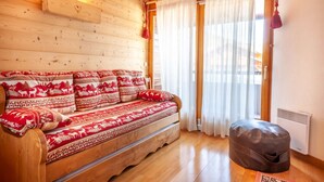 Ein Holzsofa mit gemusterten Kissen, ein kleiner Hocker und ein Fenster mit Vorhängen.
