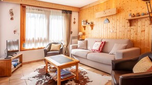 Ein gemütliches Wohnzimmer mit Holzvertäfelung, einer Couch, einem Couchtisch, einem Fernseher und einem Ledersessel.