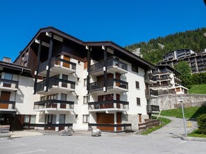 Un hôtel à plusieurs étages, doté de balcons, d’une façade en pierre et offrant une vue sur une colline boisée.