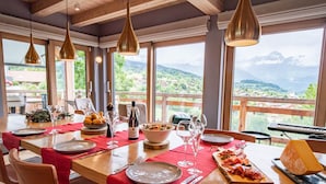 A dining table set with plates, glasses, and a variety of food items, overlooking a mountainous landscape. - Chalet Caprice, 8 people (COMBLOUX)