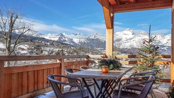 Een houten terras met tafel en stoelen, met uitzicht op een besneeuwd berglandschap.