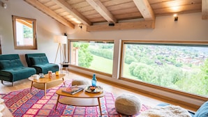 A cozy living room with a large window offering a scenic view of a village, a wooden ceiling, and a colorful rug. - Chalet Caprice, 8 people (COMBLOUX)