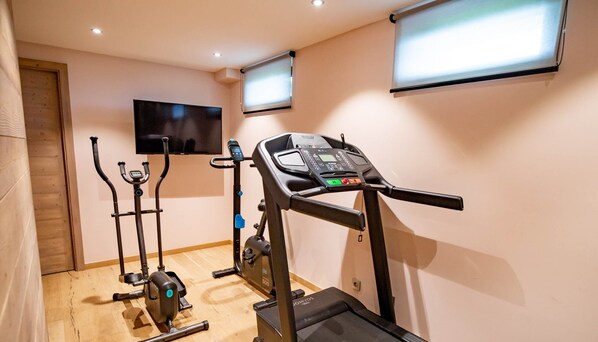 A home gym with a treadmill, elliptical, and stationary bike, a TV on the wall, and a wooden floor. - Chalet Caprice, 8 people (COMBLOUX)