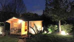 A small wooden cabin with an open door, a patio with chairs, and a well-lit interior. - Hotel Weinhaus Zum Schwarzen Bv Ren (Koblenz)