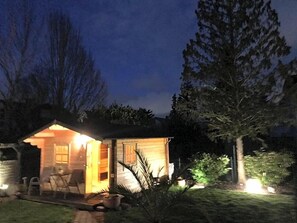 A small wooden cabin with an open door, a patio with chairs, and a well-lit interior. - Hotel Weinhaus Zum Schwarzen Bv Ren (Koblenz)