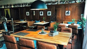 A restaurant with wooden tables and brown leather chairs, a black pendant light, and a wall of wine bottles. - Hotel Weinhaus Zum Schwarzen Bv Ren (Koblenz)