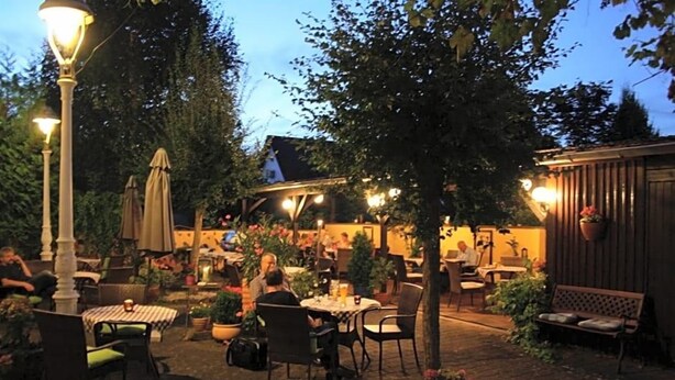 An outdoor patio area with tables and chairs, surrounded by potted plants and trees. - Hotel Weinhaus Zum Schwarzen Bv Ren (Koblenz)