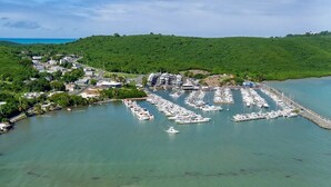 Vista aérea de un puerto deportivo con barcos amarrados, una piscina y una zona de playa con palmeras.