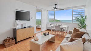 Una sala de estar moderna con televisor de pantalla plana, comedor y balcón con vistas al mar.