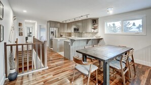 A modern kitchen with a central island, wooden flooring, and a dining area with a table and chairs. - Beautiful Canmore Home with views and walk to DT (Canmore)