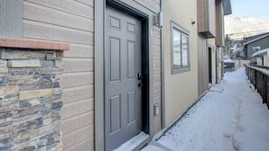A snow-covered pathway leading to a house with a stone facade and a grey door. - Beautiful Canmore Home with views and walk to DT (Canmore)