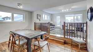 A spacious living area with a wooden dining table and chairs, a sofa, and a view of snowy mountains through large windows. - Beautiful Canmore Home with views and walk to DT (Canmore)