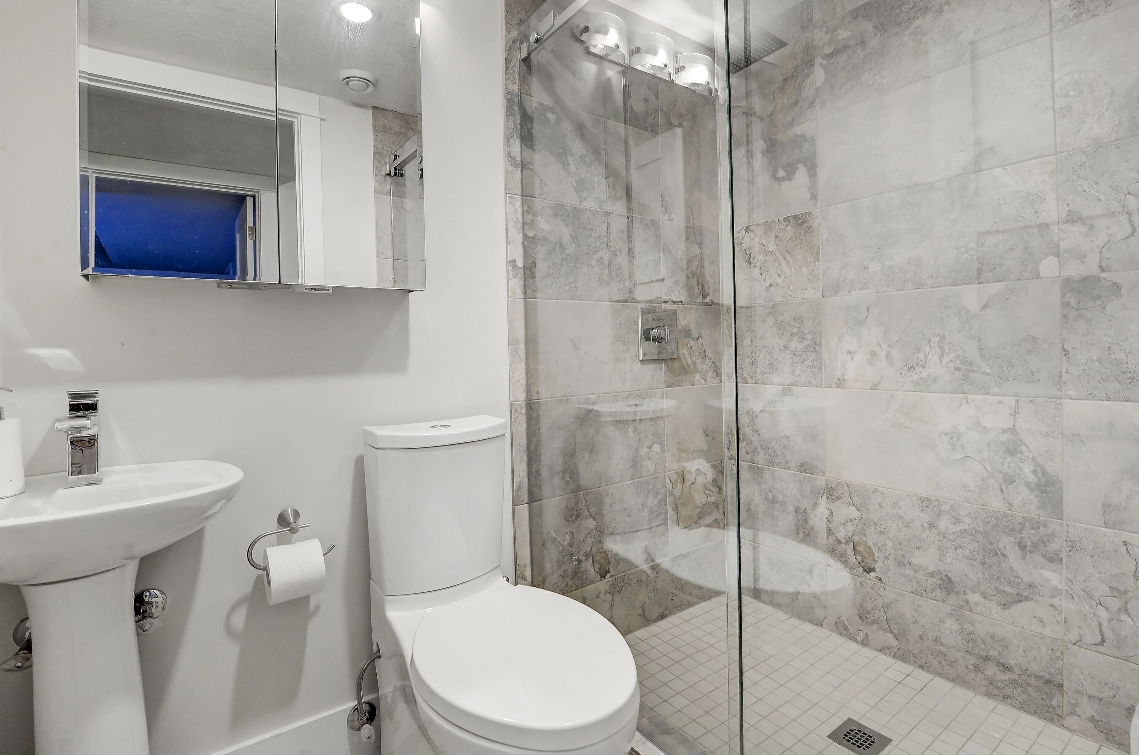 A modern bathroom with a toilet, sink, and glass shower enclosure.