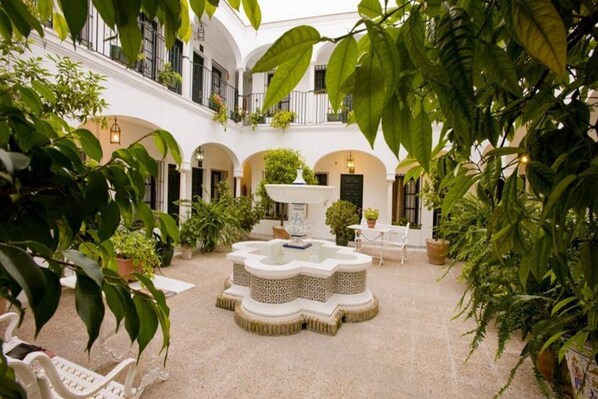 A courtyard with a central fountain, surrounded by potted plants and white furniture. - LOS Helechos (Sanlucar de Barrameda)
