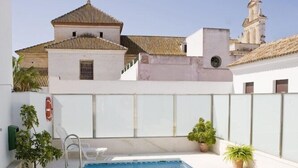 Una piscina con agua cristalina azul, rodeada de paredes blancas y algunas plantas en macetas.