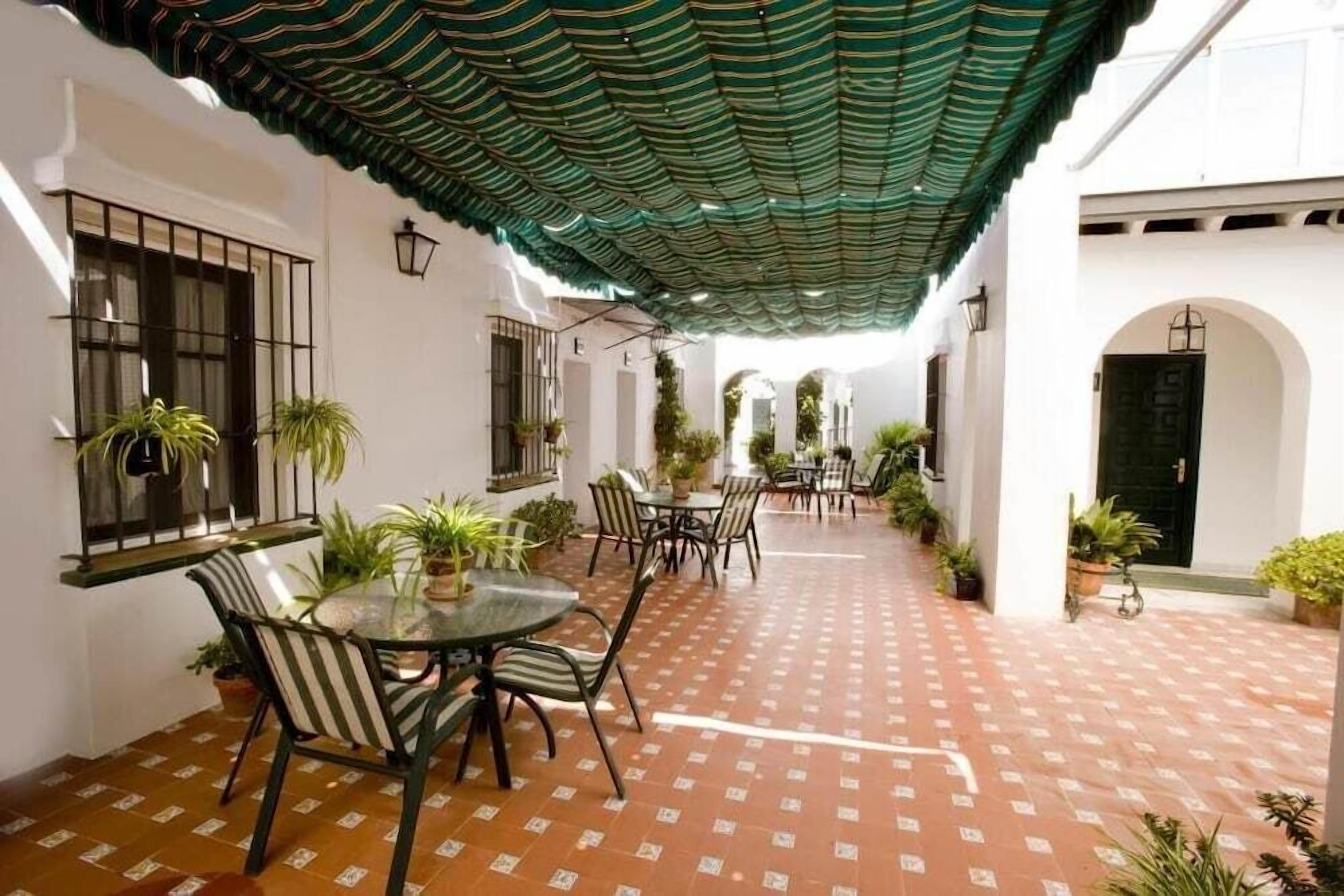 Une terrasse extérieure avec un sol à motifs, un espace salon couvert avec des chaises et une table, ainsi que des plantes en pot.