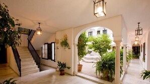Un pasillo espacioso con una escalera, plantas en macetas y vistas a un patio exterior.