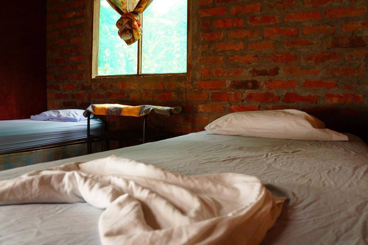 Een kamer met twee bedden, een bakstenen muur en een raam met gordijn.