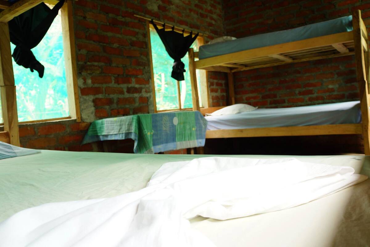 Een slaapzaal met twee stapelbedden, een bakstenen muur en een raam met gordijn.
