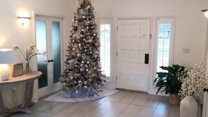 Une pièce spacieuse avec un grand plafond en bois, un sapin de Noël au centre et une porte sur le côté droit.