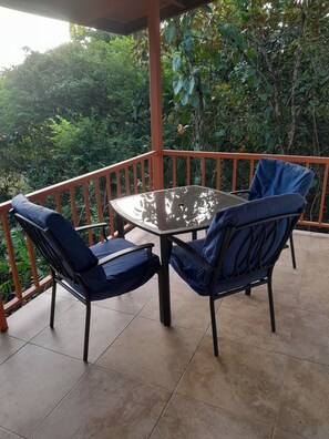 Un espace extérieur abrité, aménagé avec une table ronde et deux chaises bleues dotées de coussins.