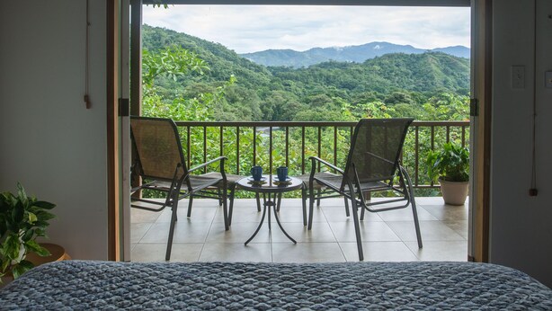 A balcony with two chairs and a table, overlooking a lush green landscape with mountains in the distance. - Torio guesthouse with panoramic view- Kokomo (Torio)