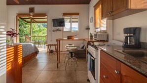 A compact kitchen with wooden cabinets, a dining area with a table and chairs, a built-in oven, and a coffee maker. - Torio guesthouse with panoramic view- Kokomo (Torio)
