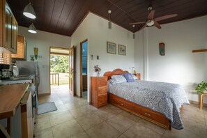 Une chambre à coucher avec un lit, des meubles en bois, un ventilateur de plafond et une vue sur l’extérieur.
