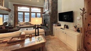 Una sala de estar acogedora con chimenea de piedra, televisor y un ventanal con vistas.